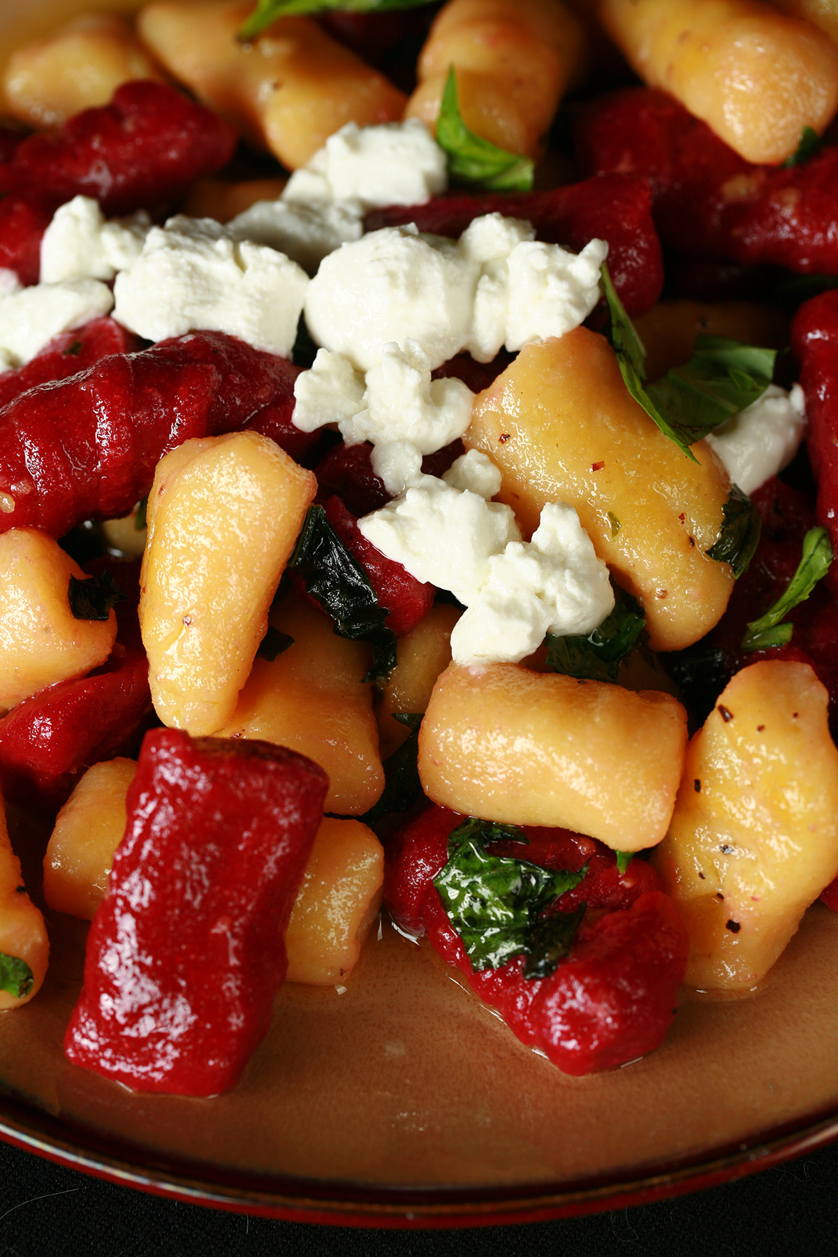 A plate of red and yellow roasted beet gnocchi. It's topped with crumbled goat cheese and fresh basil.