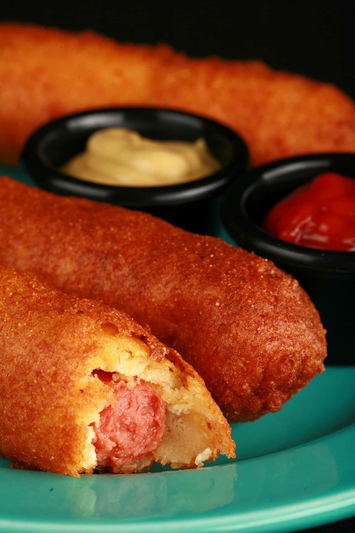 3 gluten free corn dogs on a plate with mustard and ketchup.