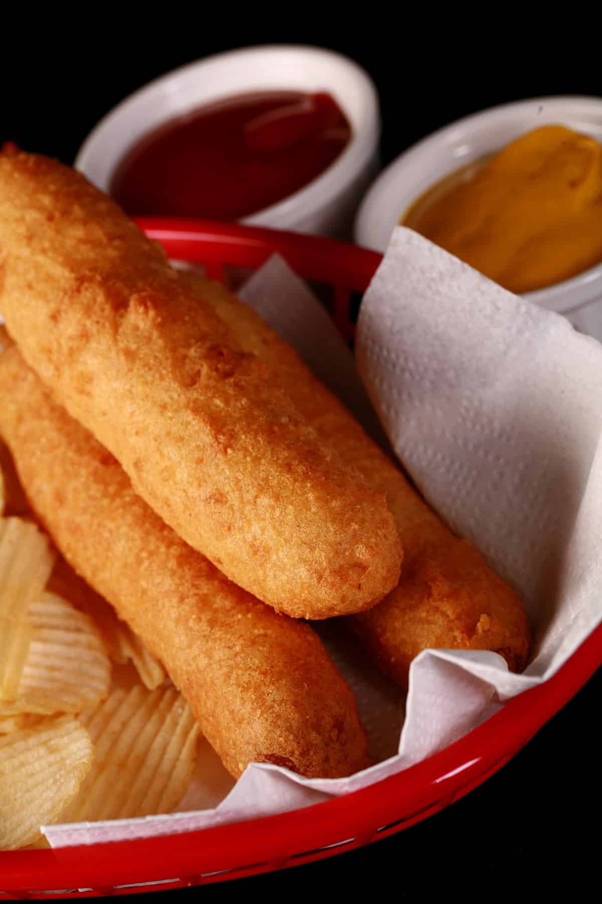3 gluten-free corndogs in a basket with mustard and ketchup.
