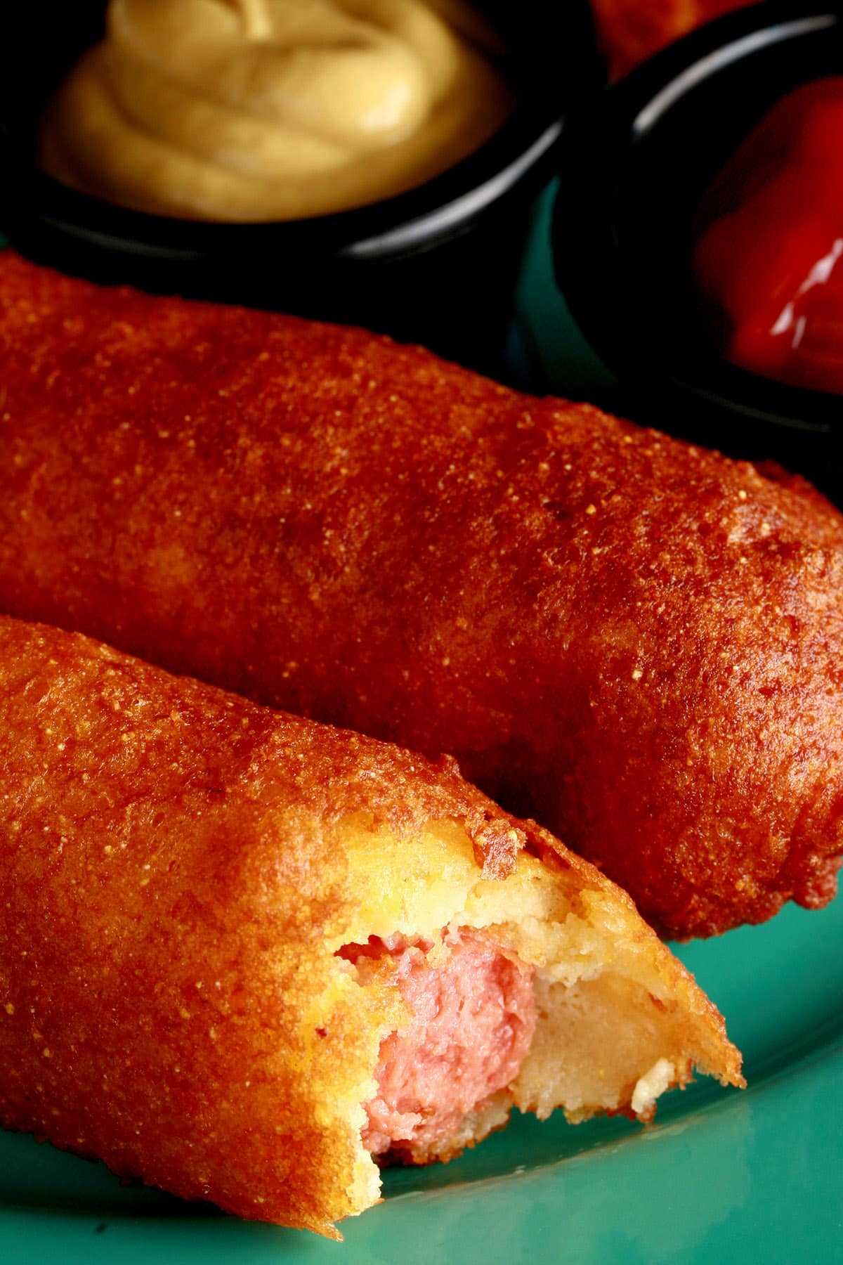 2 gluten free corn dogs on a plate with mustard and ketchup.