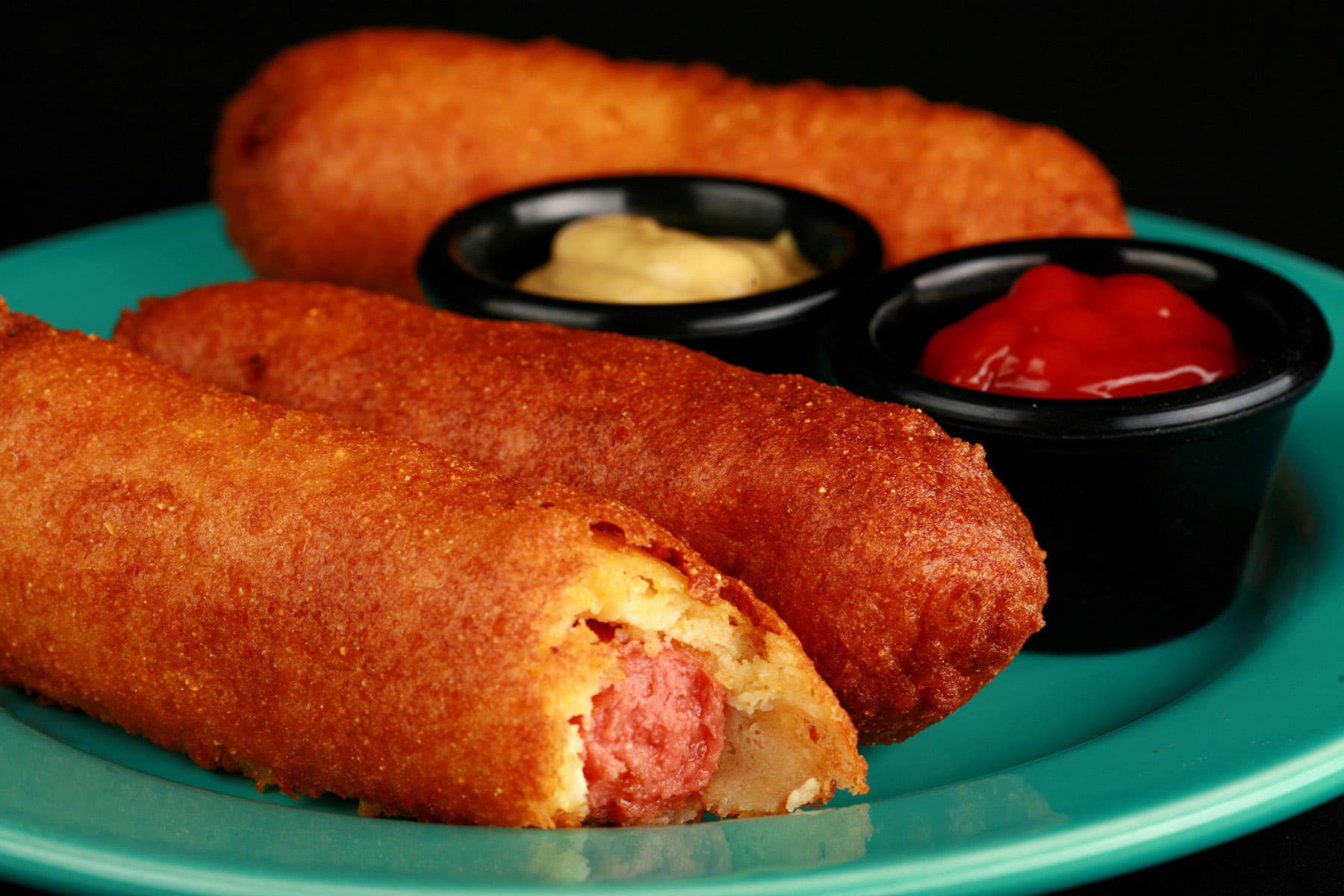 3 gluten free corn dogs on a plate with mustard and ketchup.