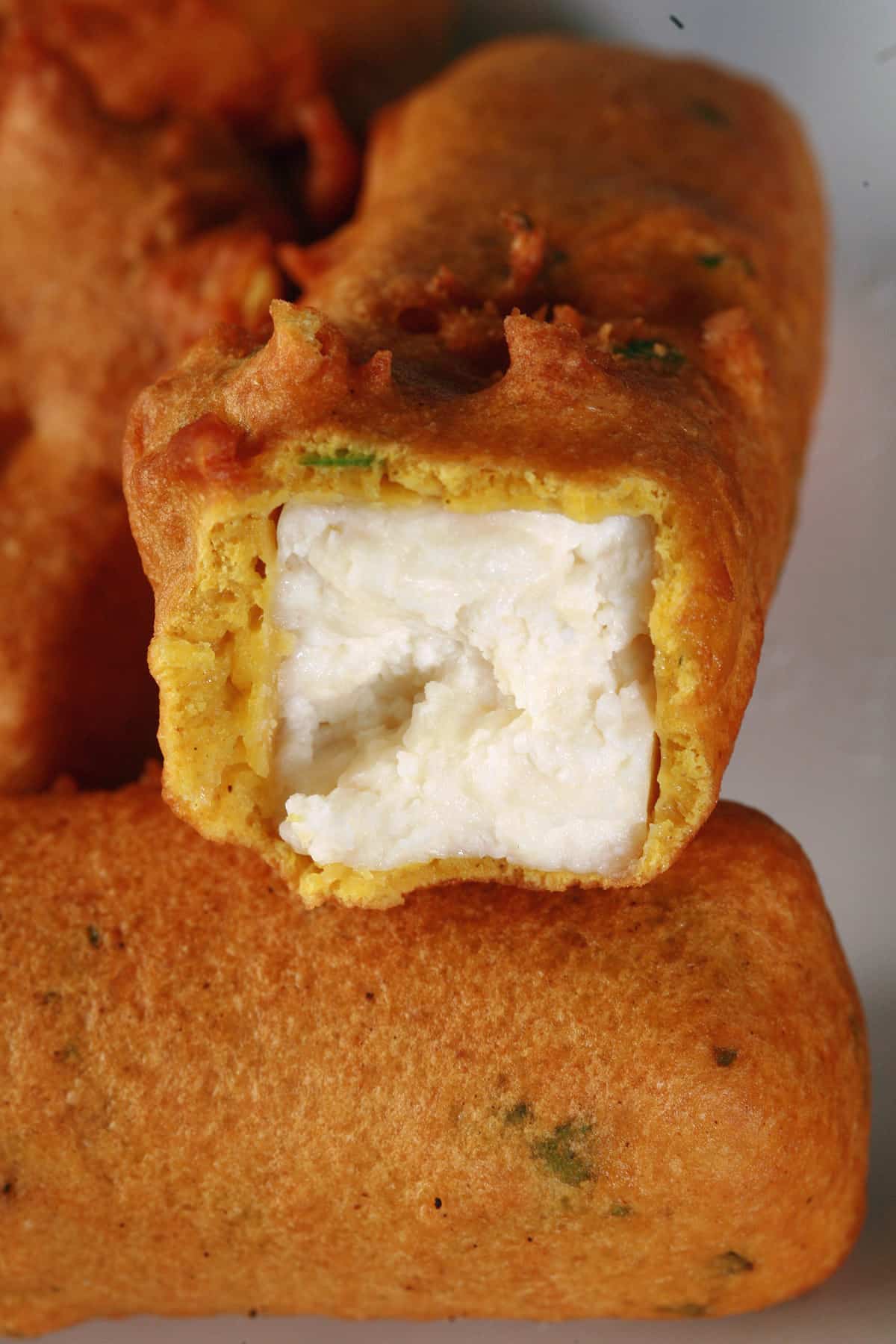 A plate of paneer pakora, with one bitten in half.