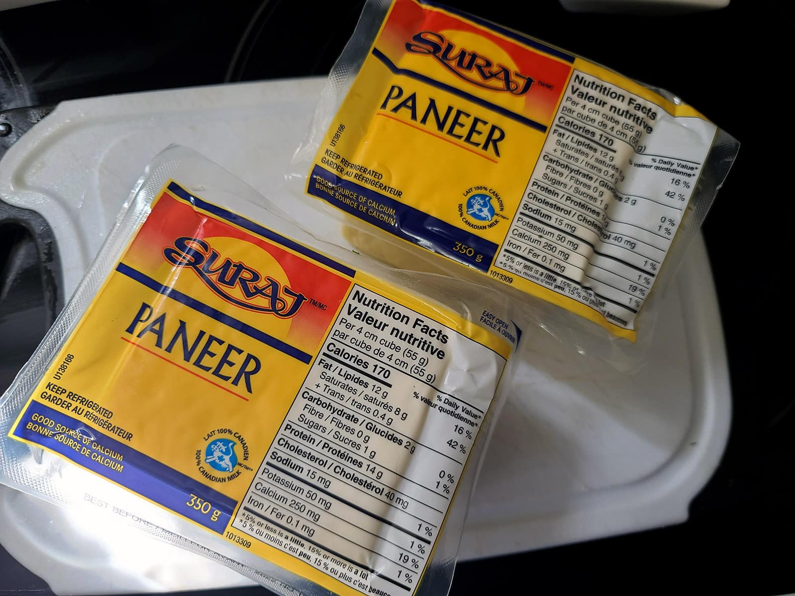 2 packages of paneer on a cutting board.