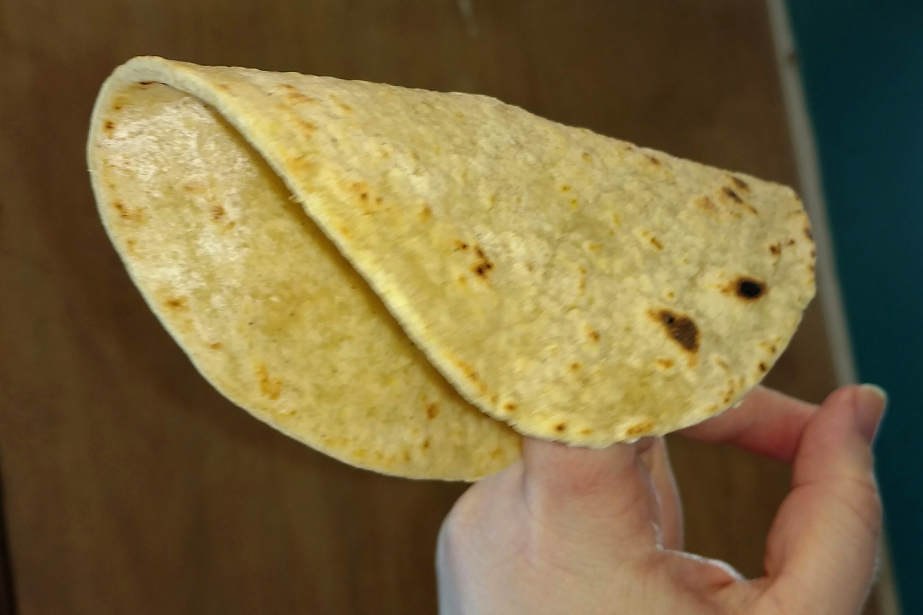 a yellow tortilla is folded over a pointed finger. It is visibly soft.