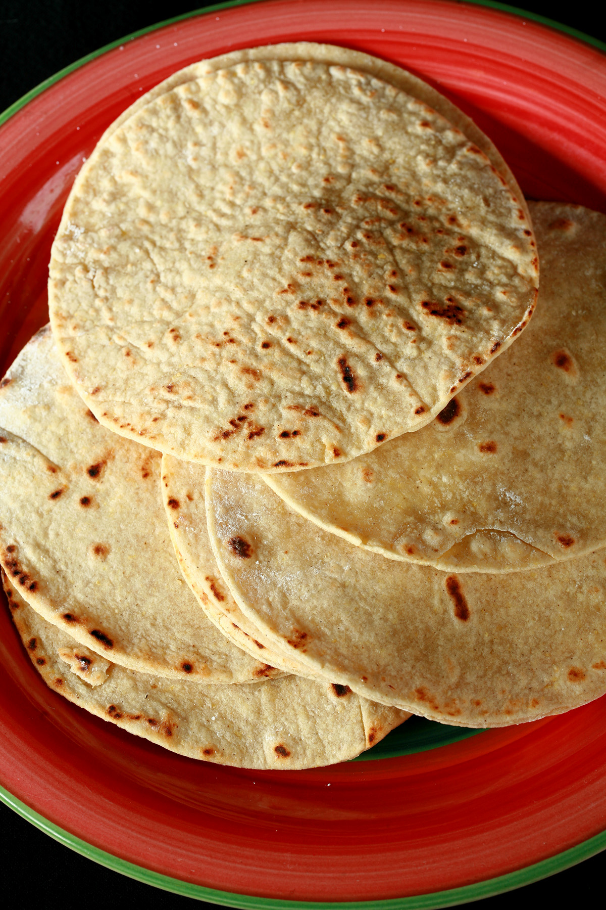 A red plate with shrimp tacos. The tacos are made from gluten-free hybrid tortillas, and look like a more yellow version of flour tortillas.