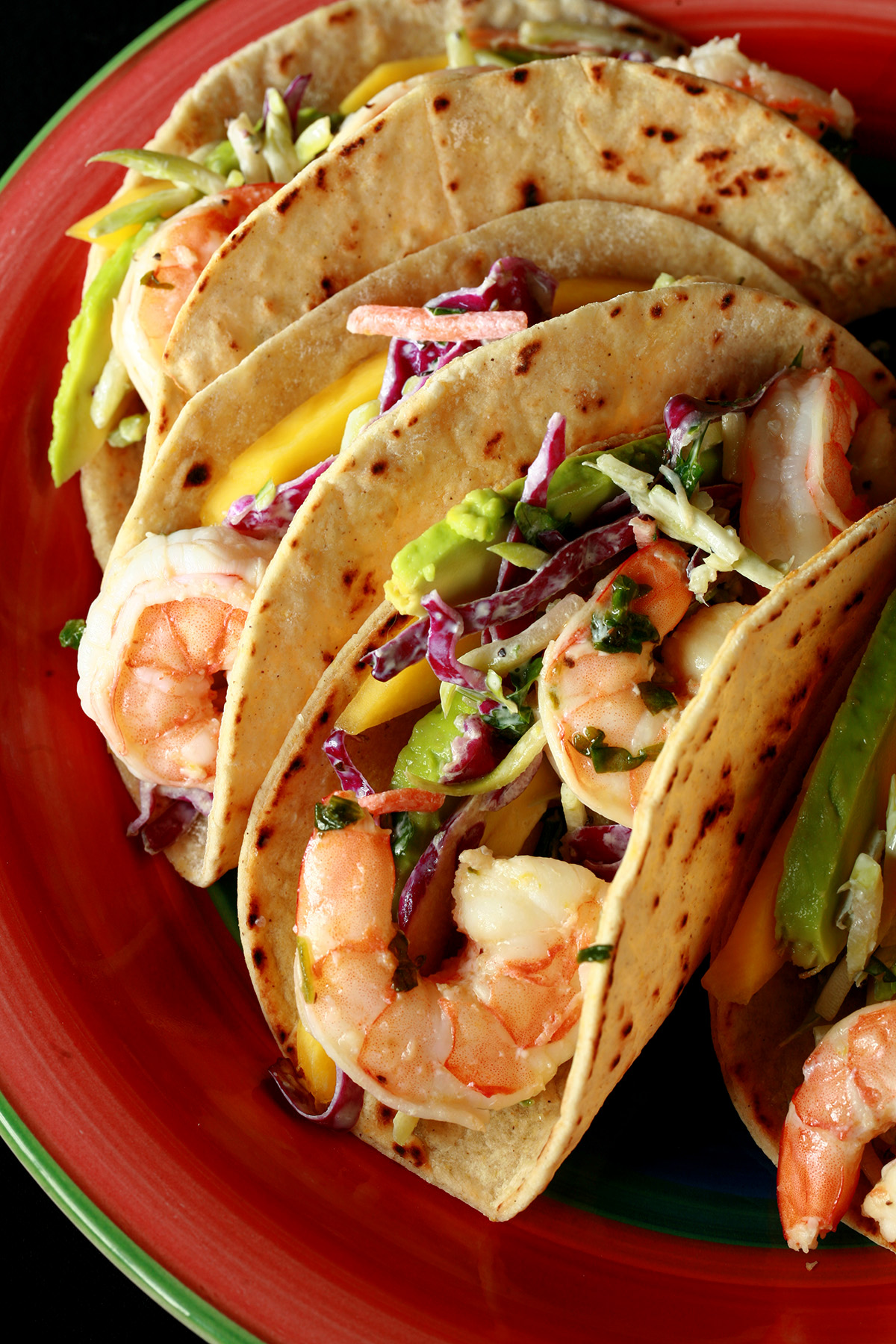 A red plate with shrimp tacos. The tacos are made from gluten-free hybrid tortillas, and look like a more yellow version of flour tortillas.