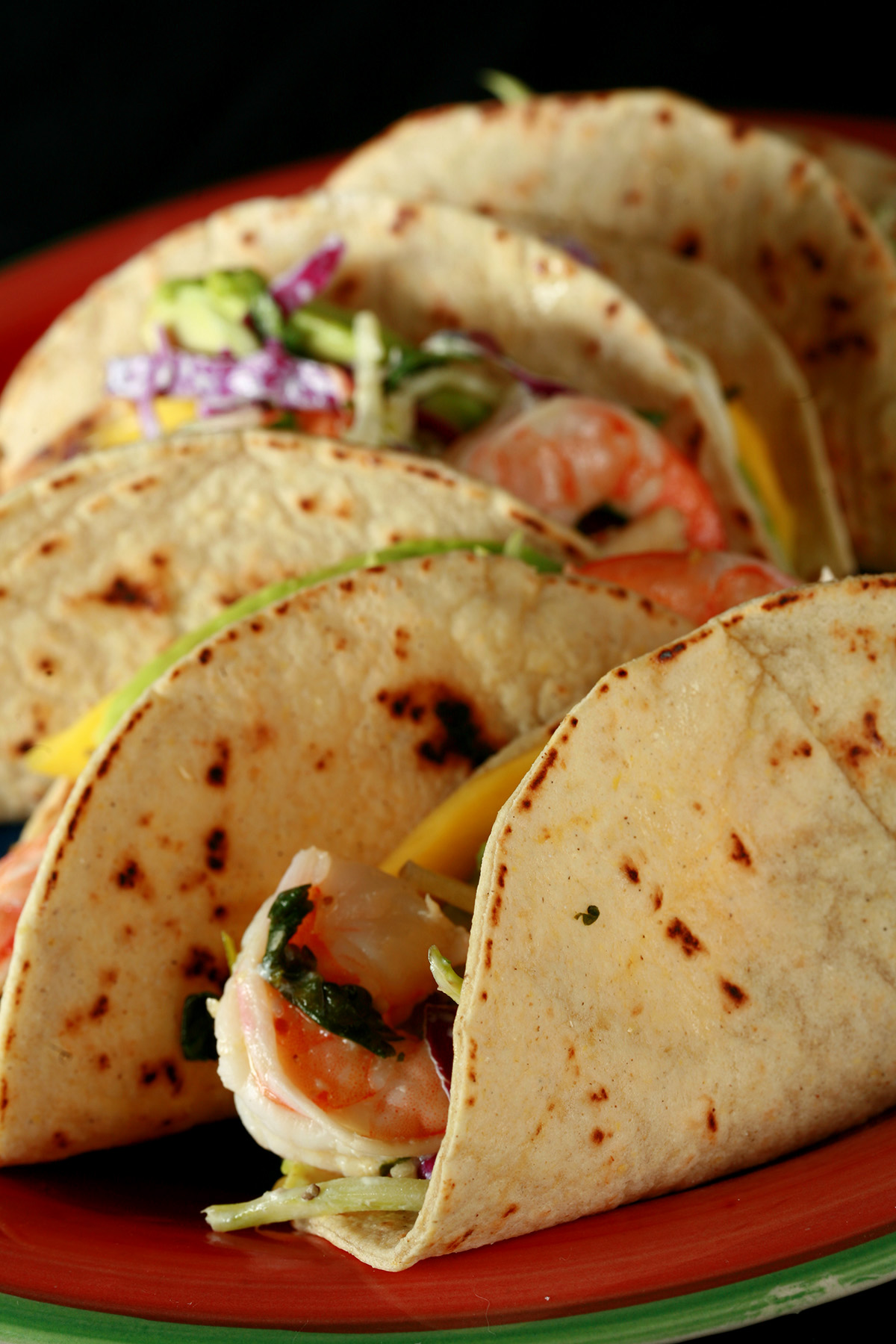 A red plate with shrimp tacos. The tacos are made from gluten-free hybrid tortillas, and look like a more yellow version of flour tortillas.