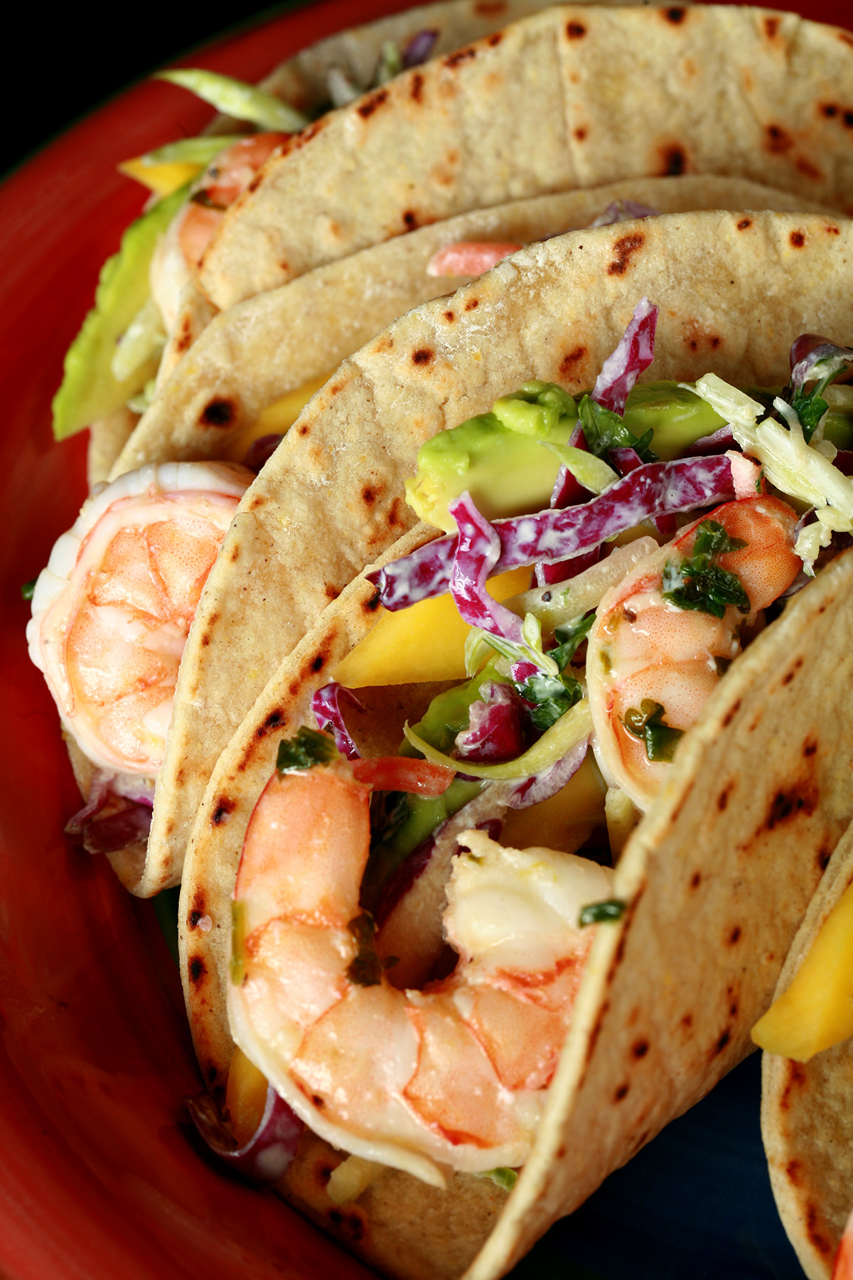 A red plate with shrimp tacos. The tacos are made from gluten-free hybrid tortillas, and look like a more yellow version of flour tortillas.