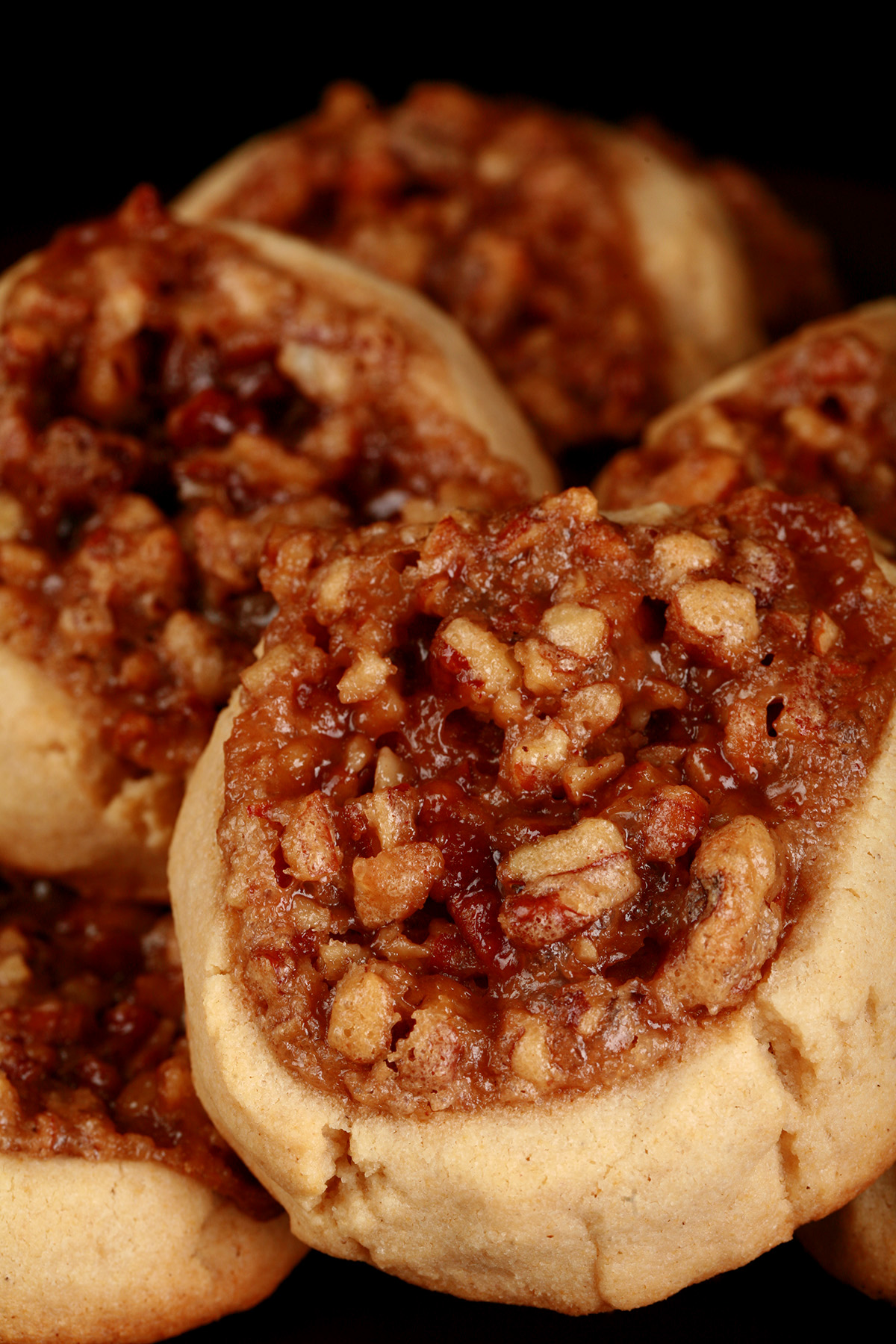 Several Gluten-Free Pecan Pie cookies on a white plate. They are golden brown, with a pecan and brown sugar topping.