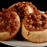 Several Gluten-Free Pecan Pie cookies on a white plate. They are golden brown, with a pecan and brown sugar topping.