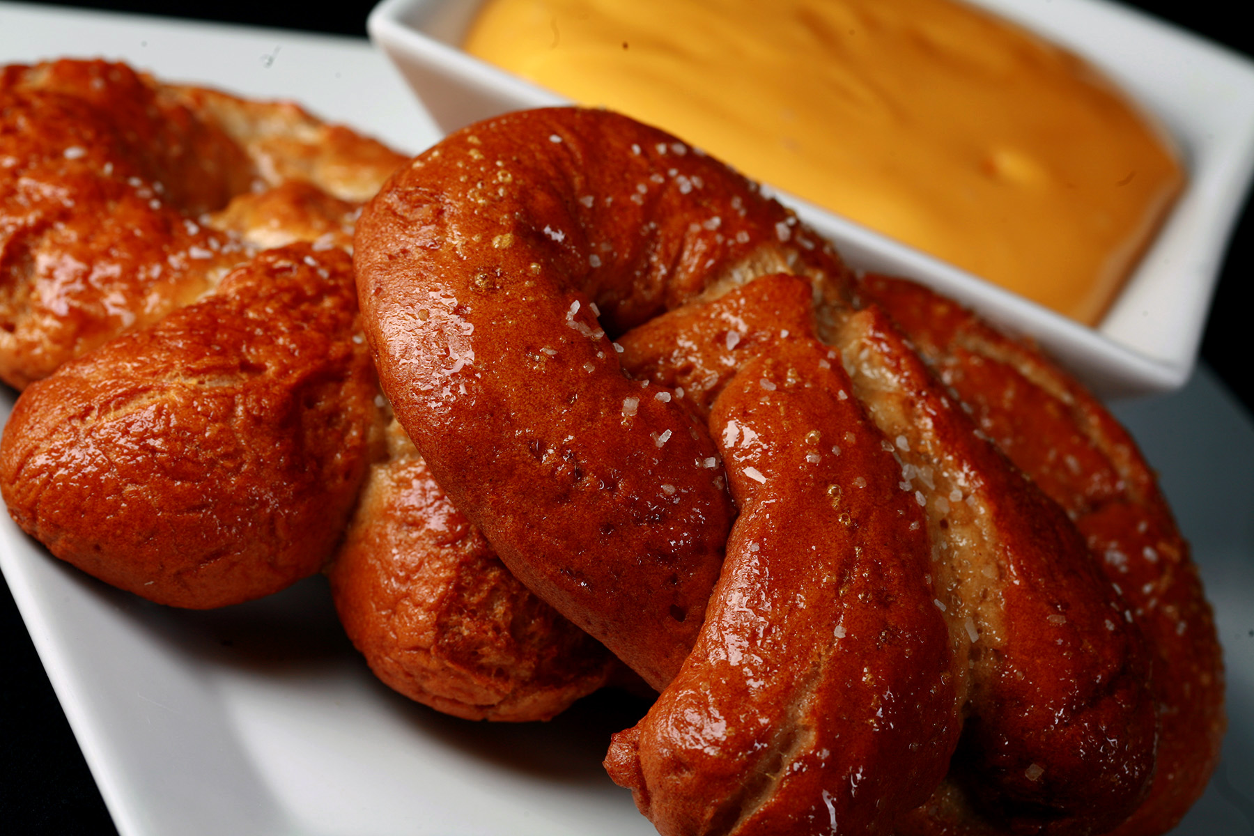 2 soft gluten-free pretzels on a plate, beside a bowl of mustard-cheddar dip.