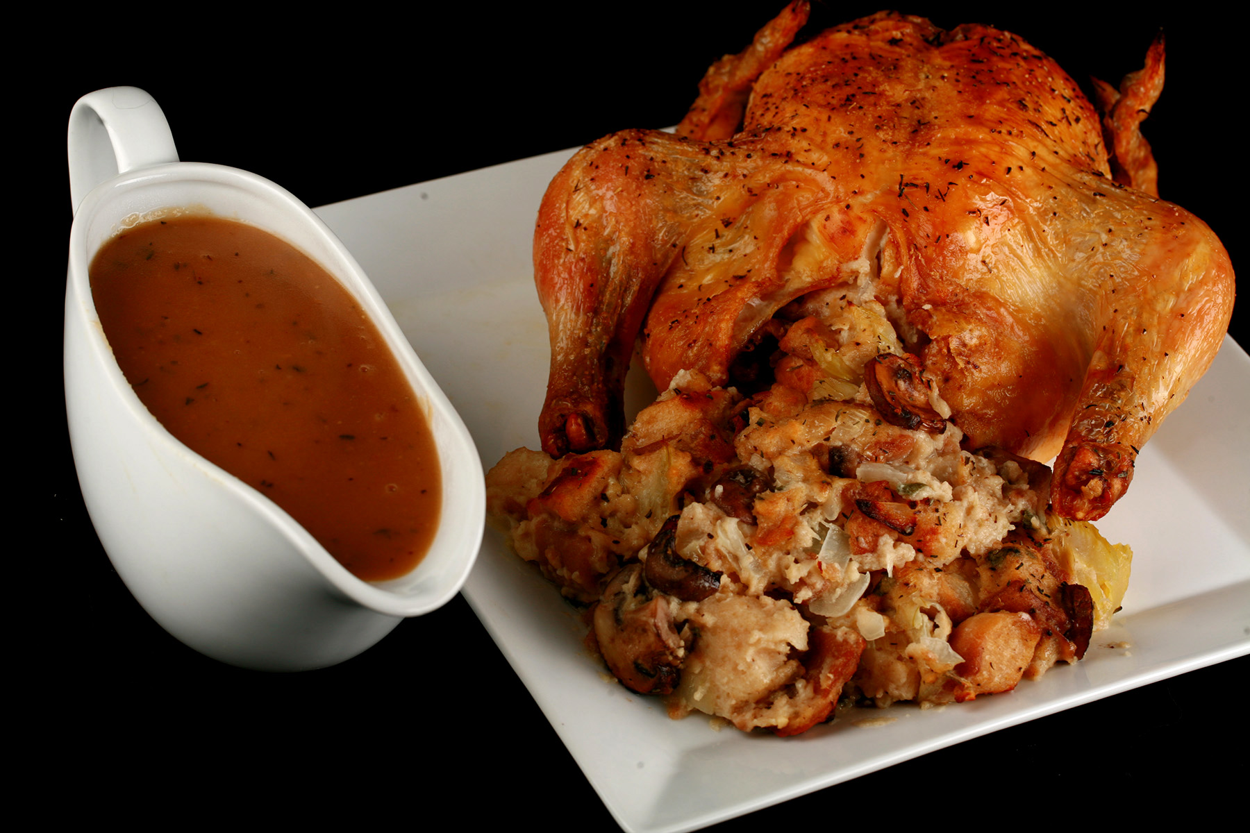A small roasted turkey on a platter, with gluten-free stuffing spilling out from it. There is a gravy boat with gluten-free gravy in it, next to the turkey.