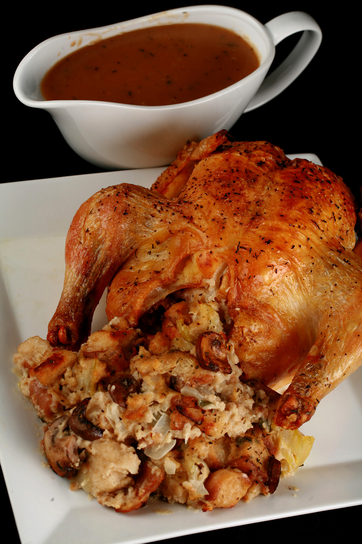 A small roasted turkey on a platter, with gluten-free stuffing spilling out from it. There is a gravy boat with gluten-free gravy in it, next to the turkey.