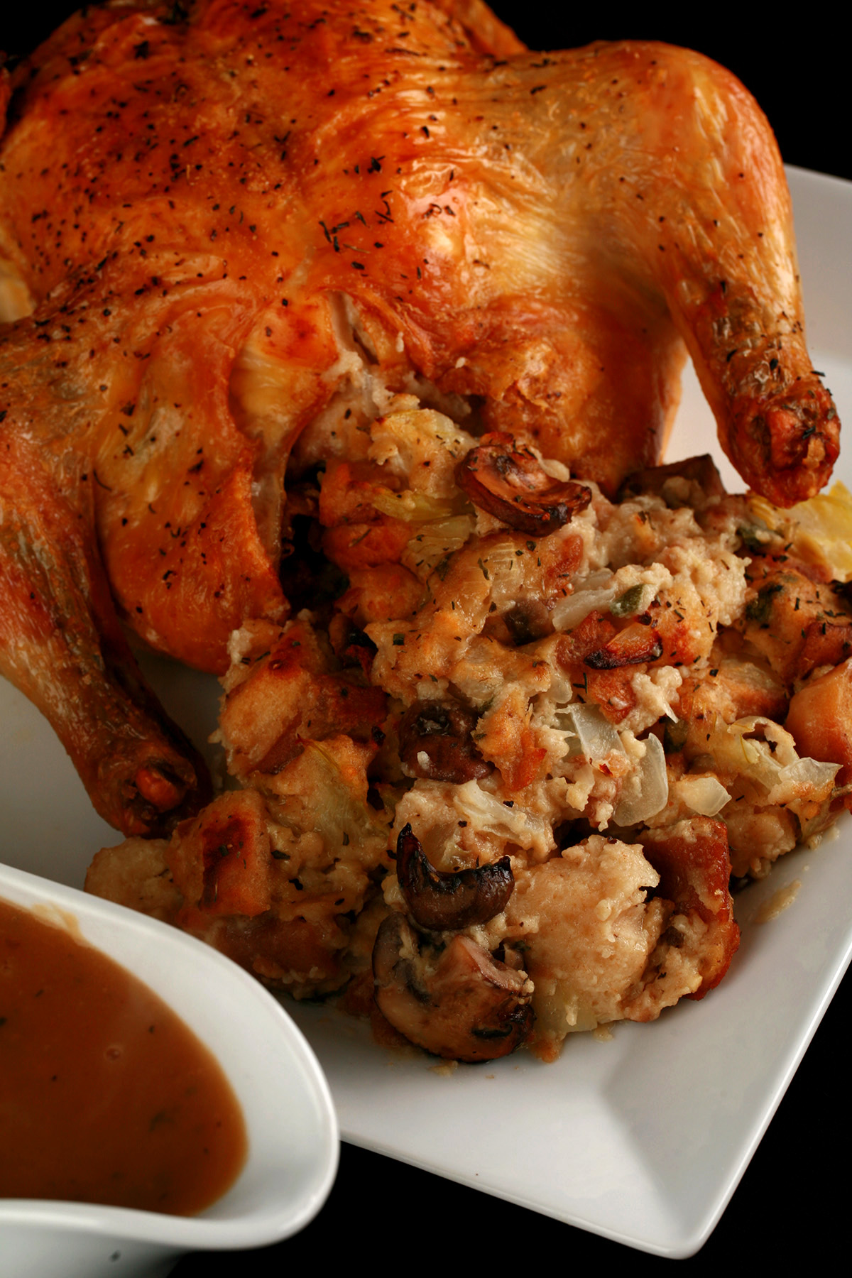 A small roasted turkey on a platter, with gluten-free stuffing spilling out from it. There is a gravy boat with gluten-free gravy in it, next to the turkey.