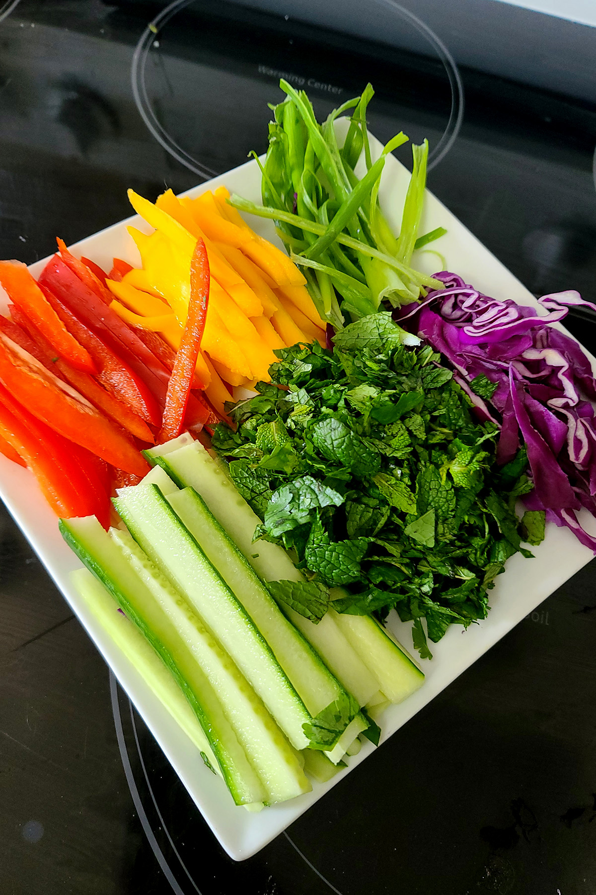 A white plate with slices of red pepper, mango, green onion, and cucumber, along with red cabbage and cilantro - mint mixture.