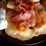 A plate of gluten-free pierogi, topped with bacon, fried onions, and sour cream.