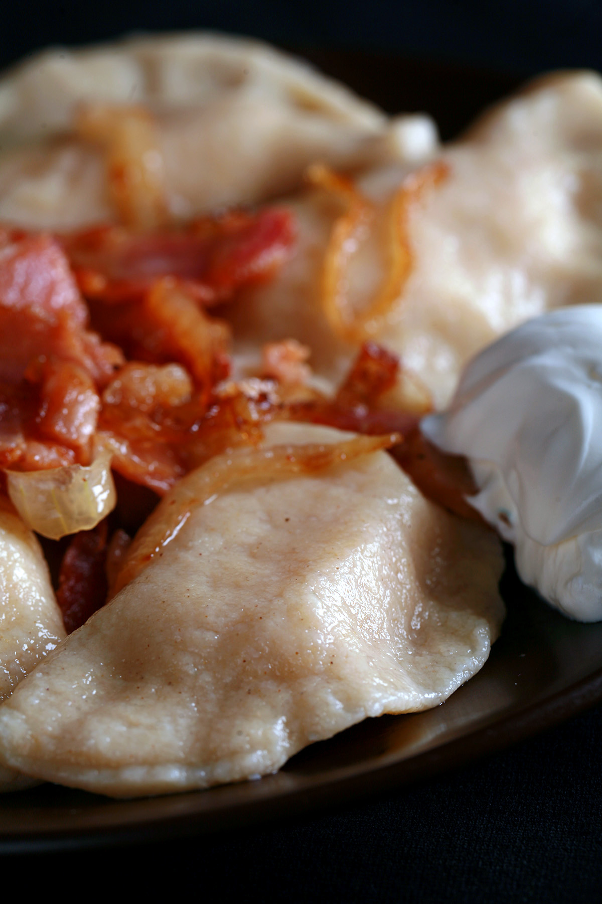 A plate of gluten-free perogies, topped with bacon, fried onions, and sour cream.