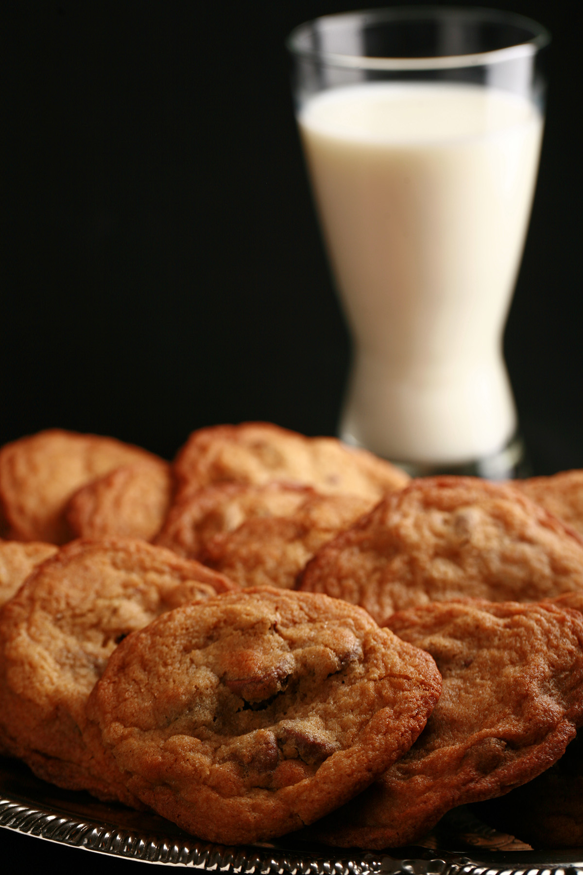 A plate of chewy gluten free chocolate chip cookies, with a tall glass of milk.