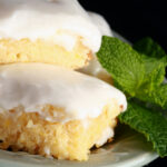 A plate of frosted chewy gluten free lemon bars, garnished with mint leaves.