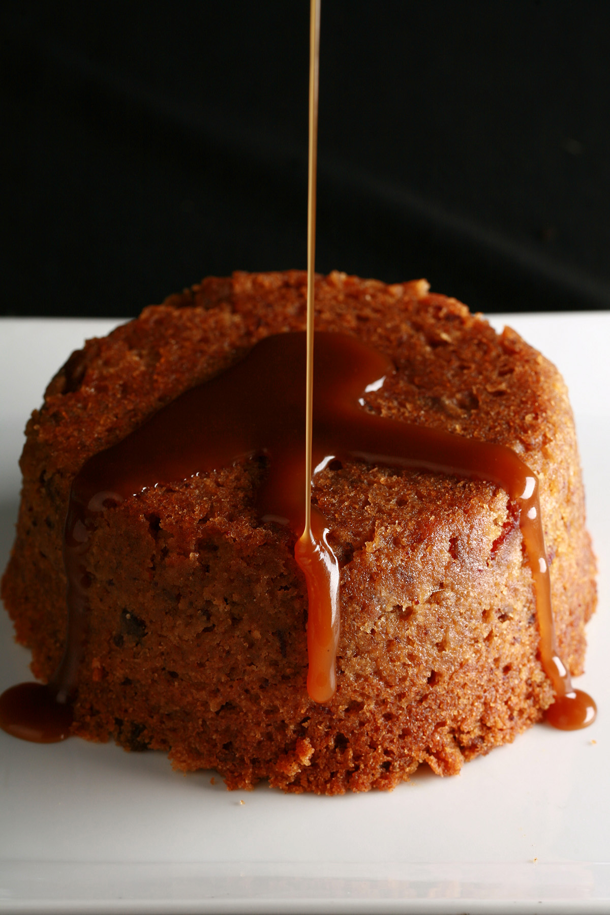 A gluten-free sticky toffee pudding with toffee sauce being poured over it.