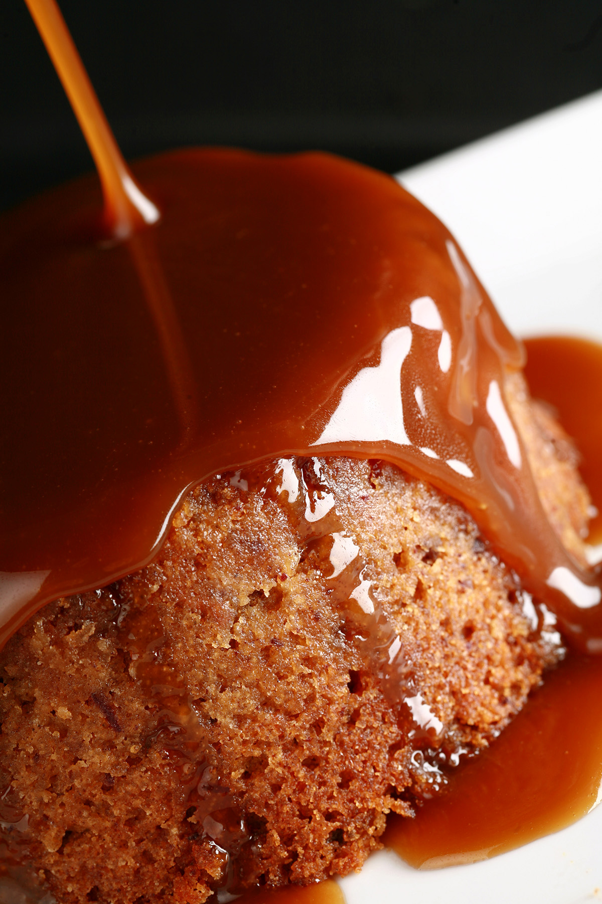 A gluten-free sticky date pudding with toffee sauce being poured over it.