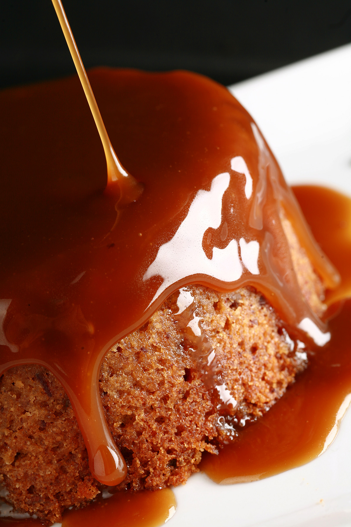A gluten free sticky toffee pudding with toffee sauce being poured over it.