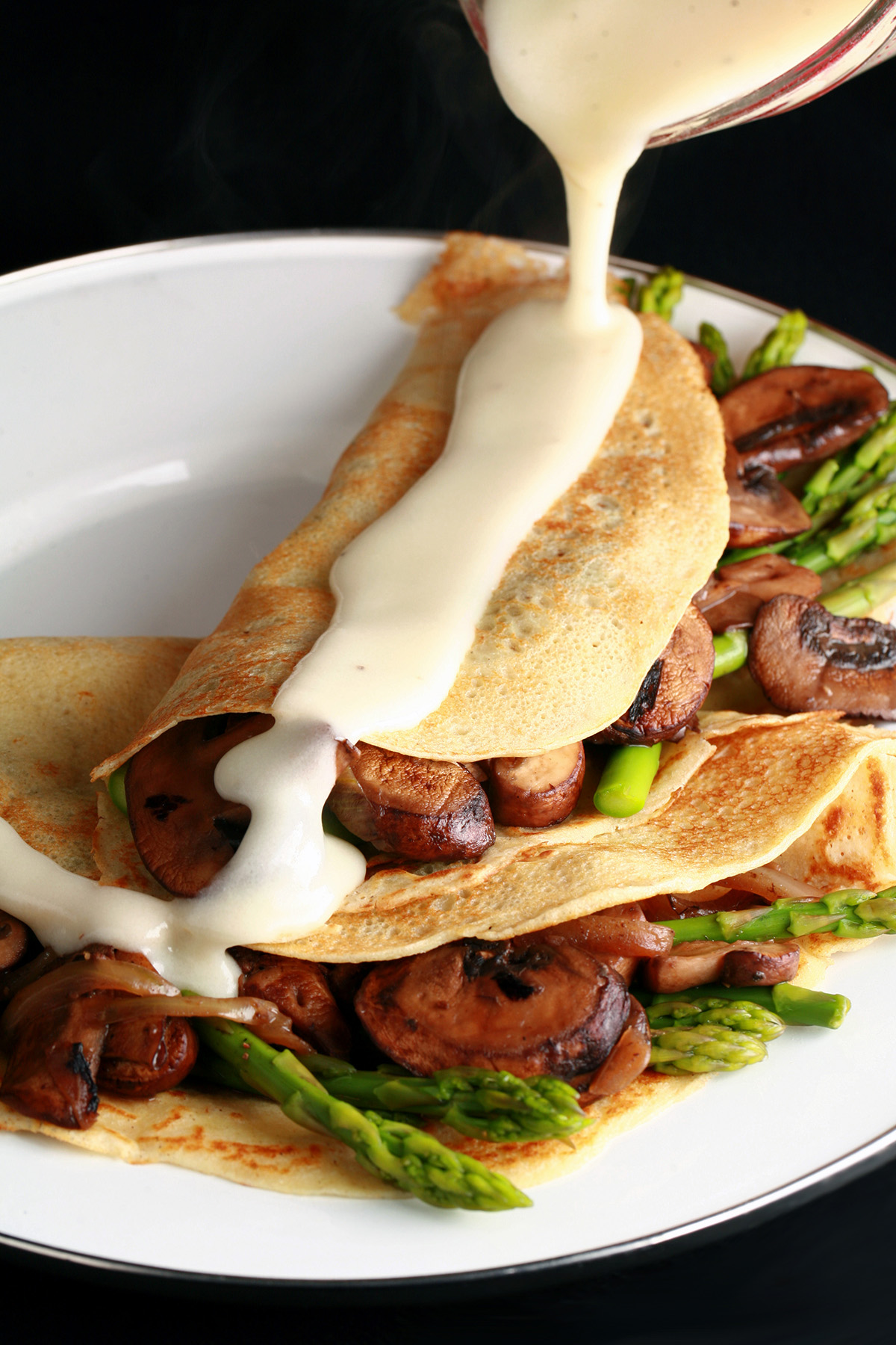 Two gluten free crepes stuffed with mushrooms and aspagus, drizzled with Swiss cheese sauce.