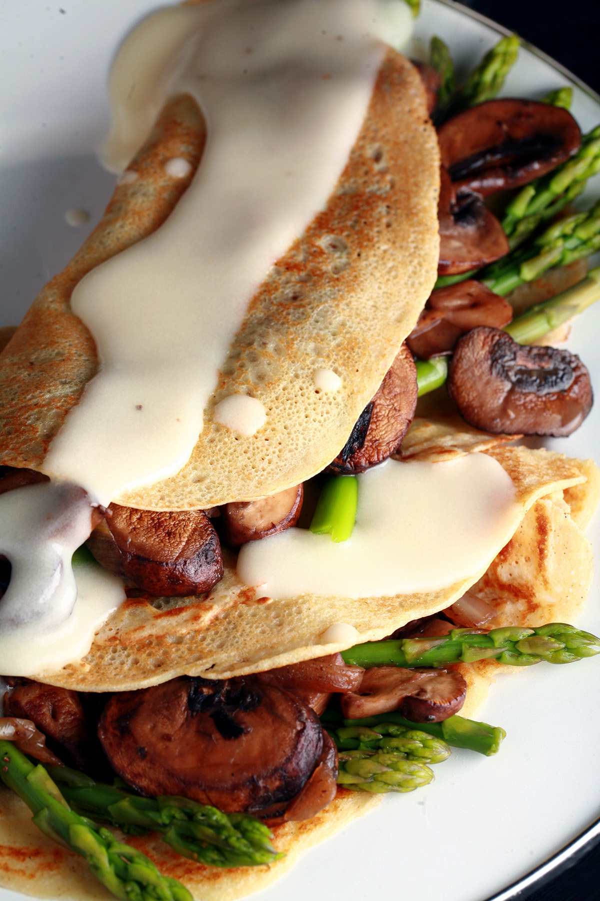 Two gluten free crepes stuffed with mushrooms and aspagus, drizzled with Swiss cheese sauce.