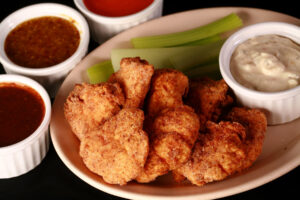 A plate of deep fried gluten-free chicken nuggets, celery, and dip.