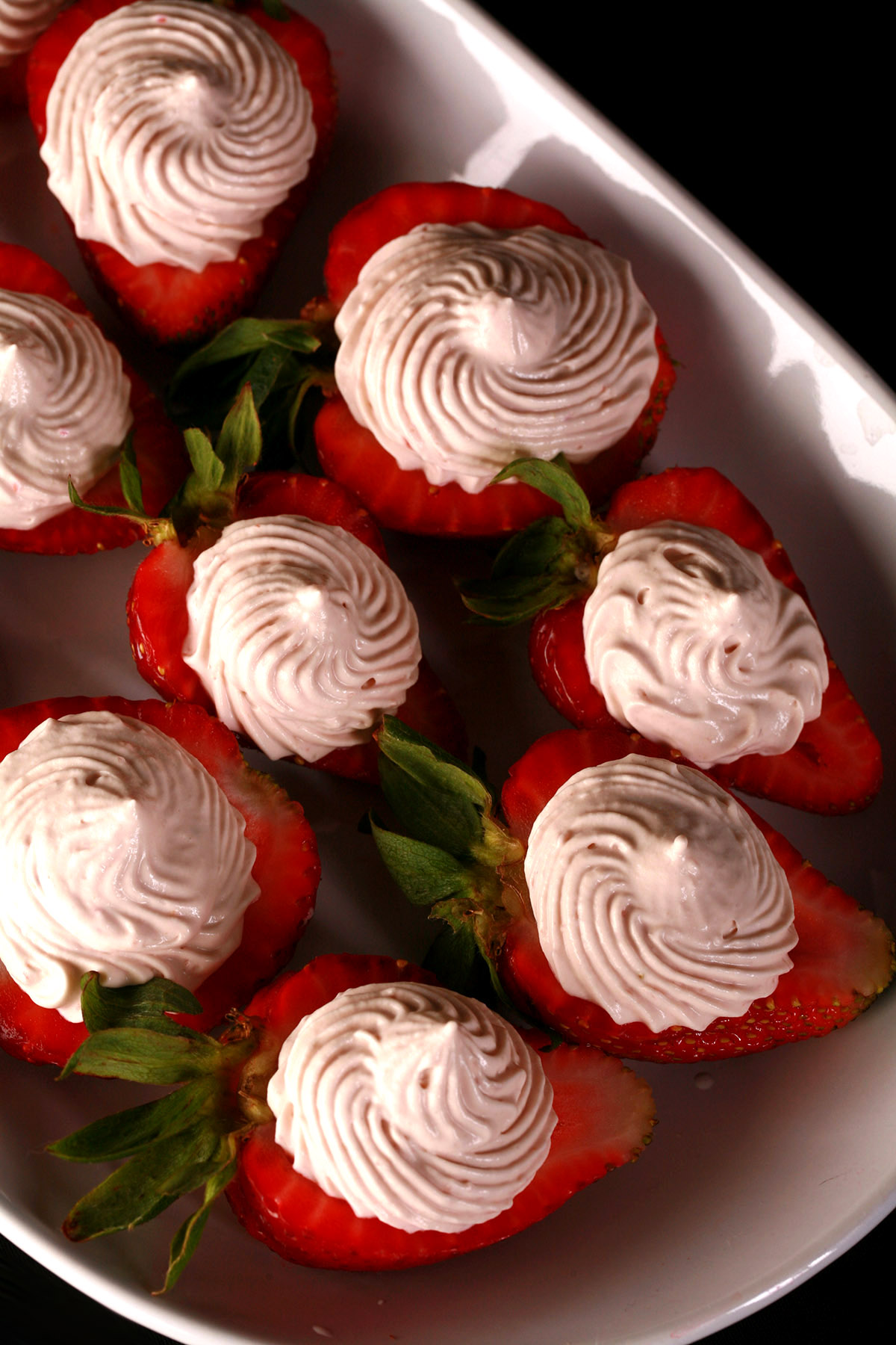 A white plate with deviled strawberries, filled with a cream cheese and balsamic vinegar whipped cream.