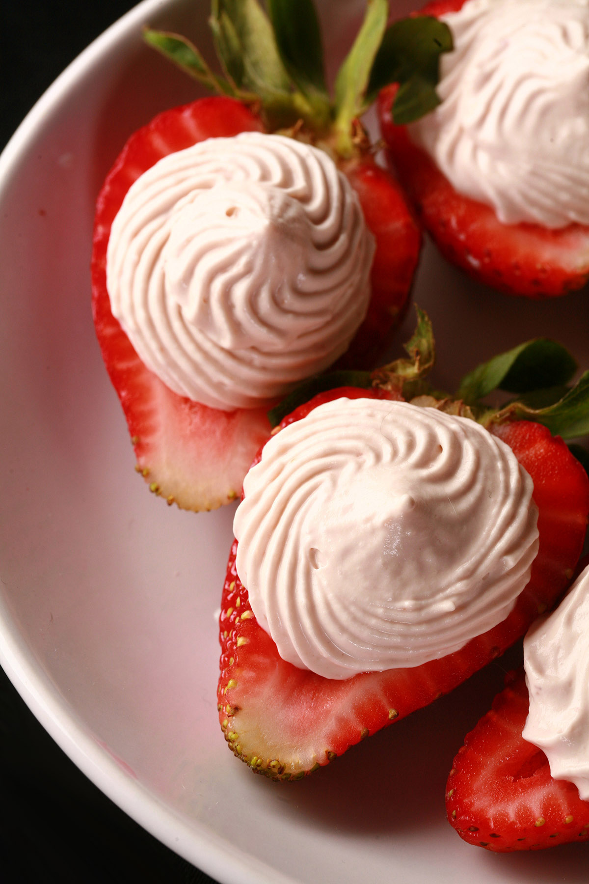 A white plate with deviled strawberries, filled with a cream cheese and balsamic vinegar whipped cream.