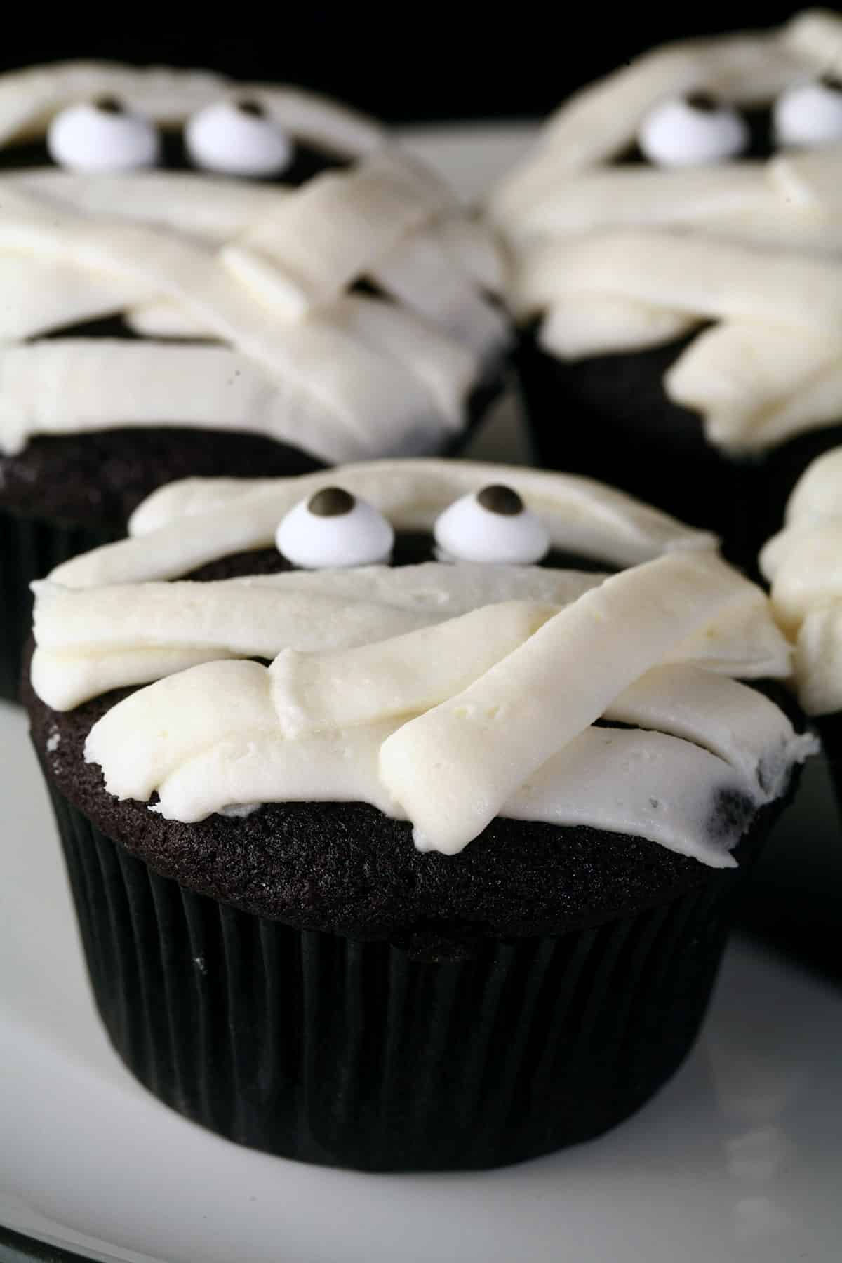 4 halloween cupcakes decorated to look like mummies. The base is a black velvet cupcake.