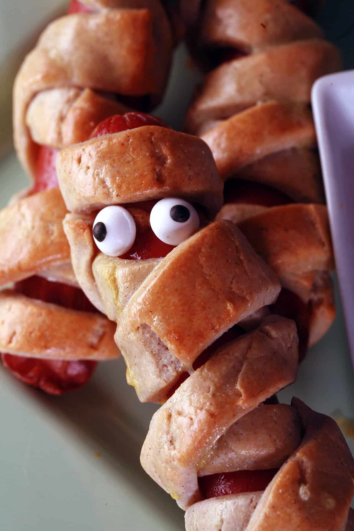 Several gluten free mummy dogs on a plate. Each have 2 candy eyes.