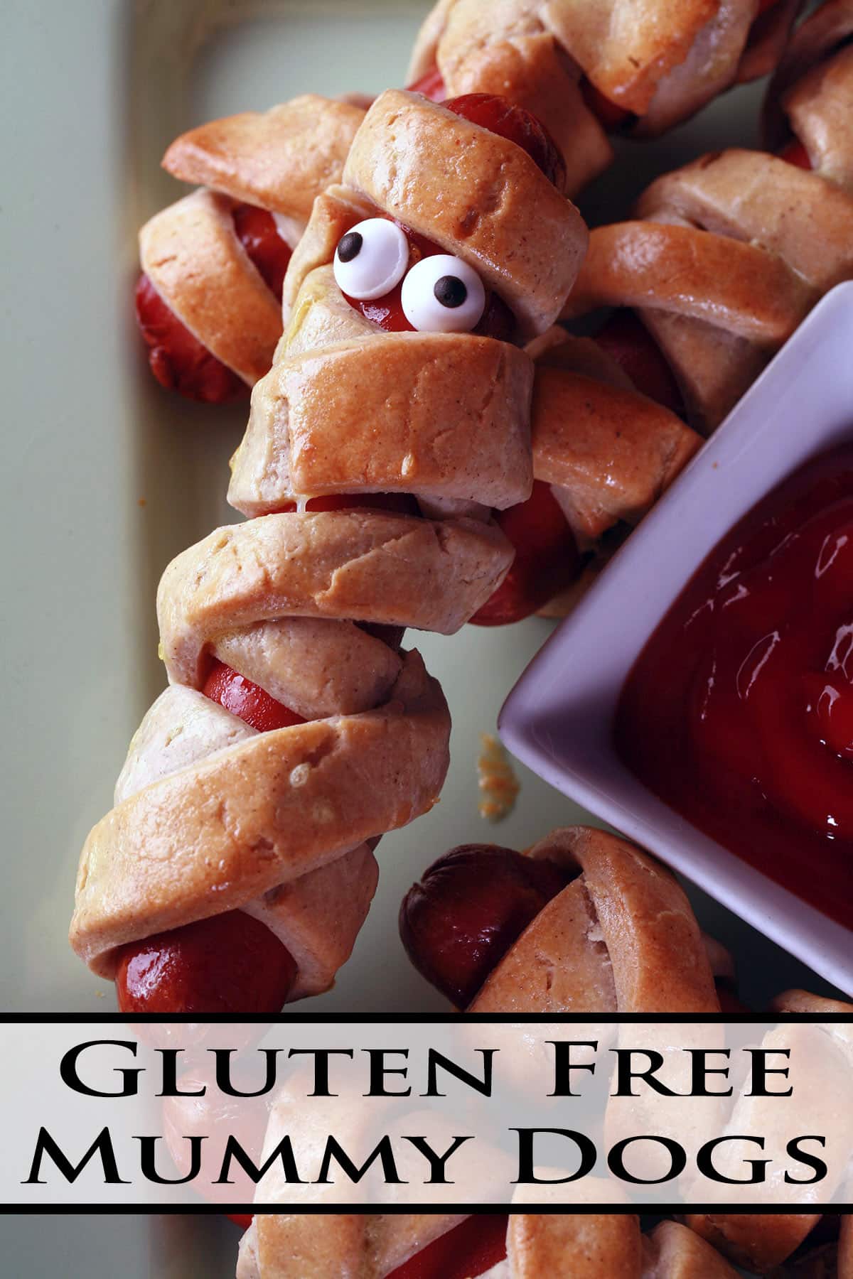 Several gluten free mummy dogs on a plate. Each have 2 candy eyes.