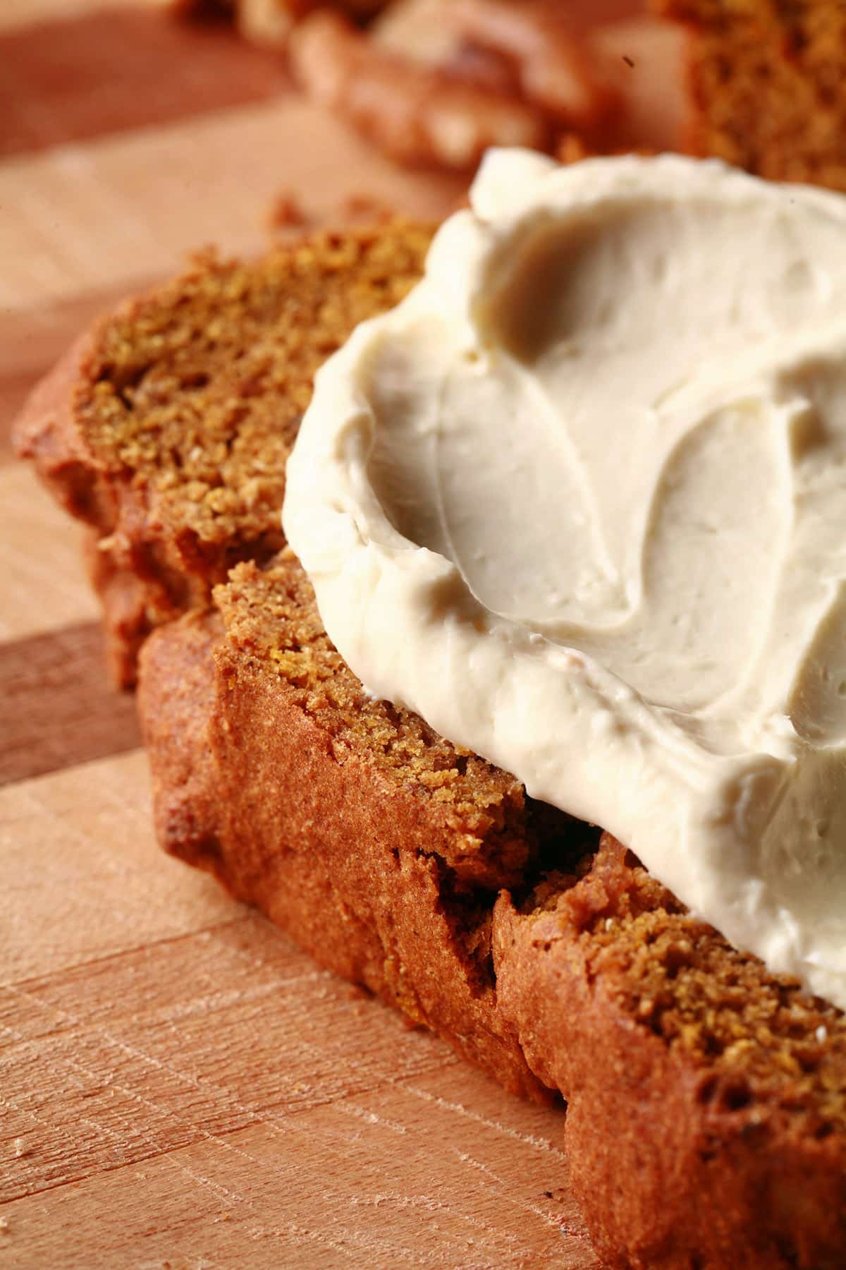 A slice of gluten free pumpkin spice bread on a cutting board, sliced. The slice is spread with cream cheese.