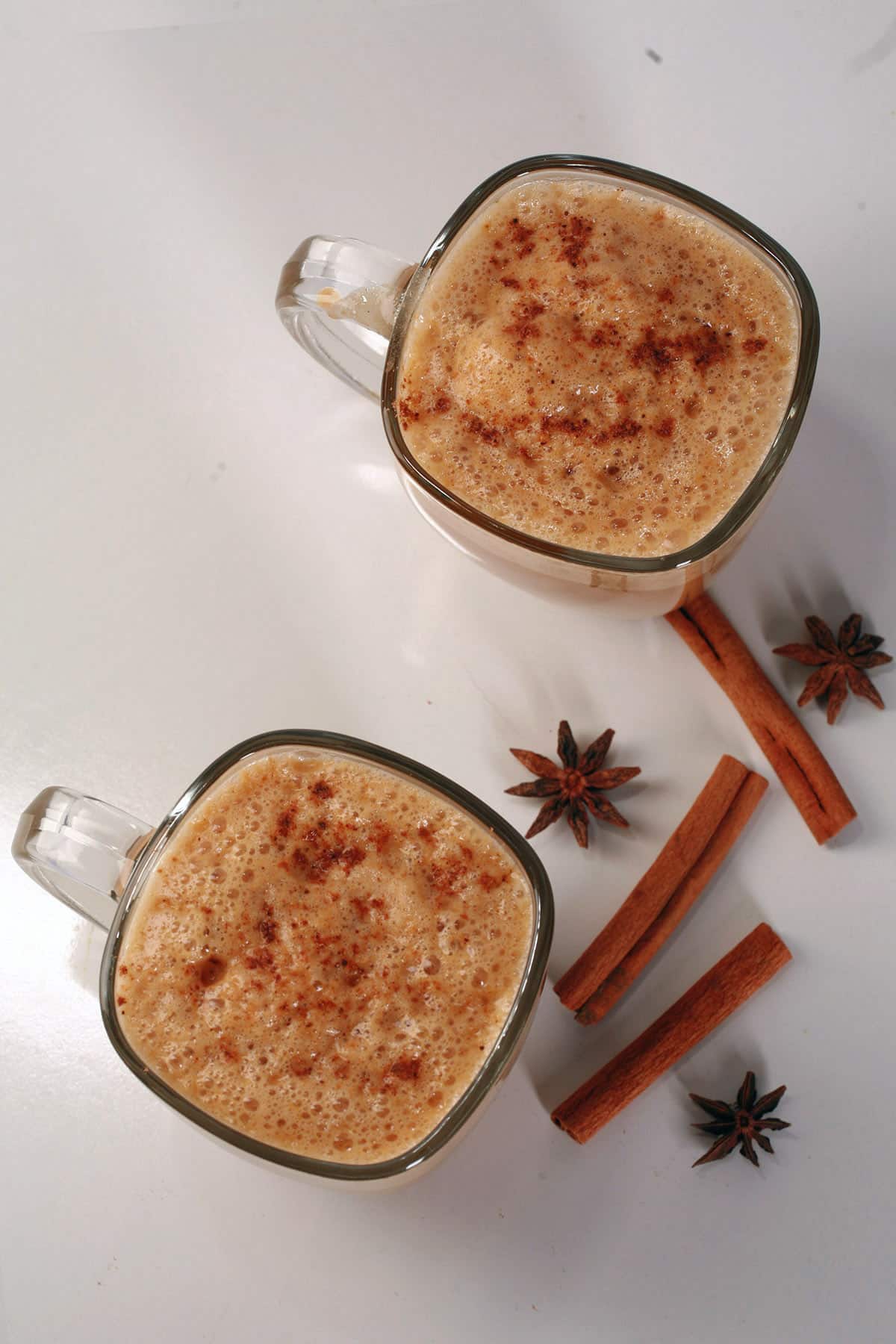2 Pumpkin Chai Lattes in glass mugs, with cinnamon sticks and star anise around them.