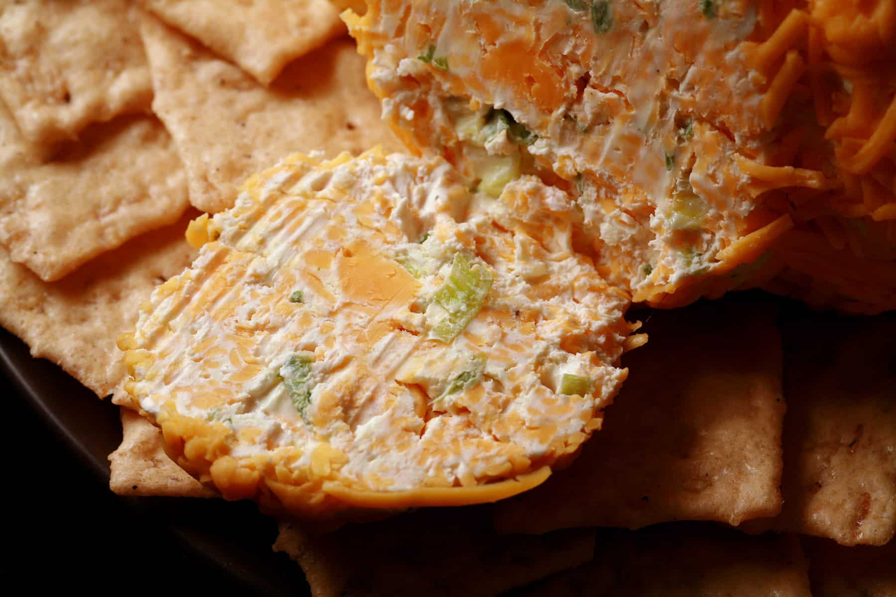 A slice of cheese ball, showing cream cheese, cheddar and green onions.