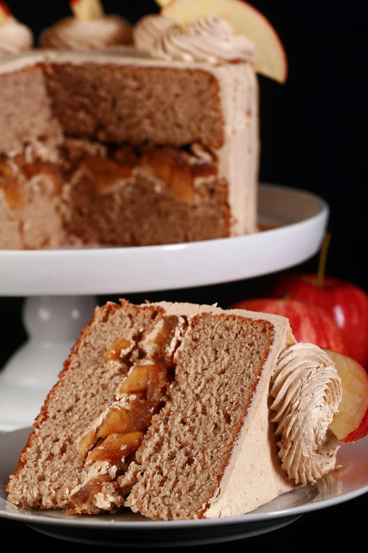 A slice of gluten-free apple cake on a plate in front of the whole gluten free apple cake.