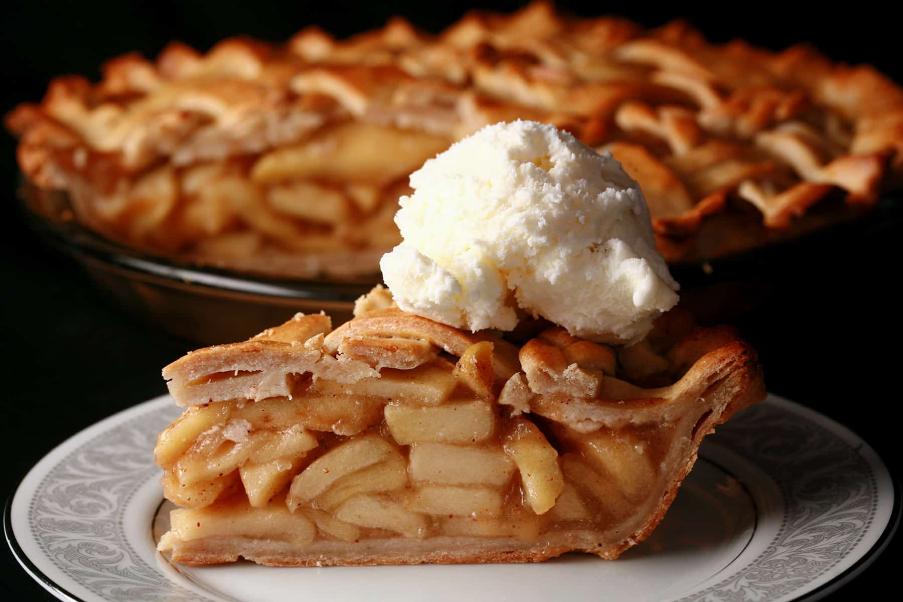 A slice of gluten free apple pie, in front of the whole gluten-free pie.