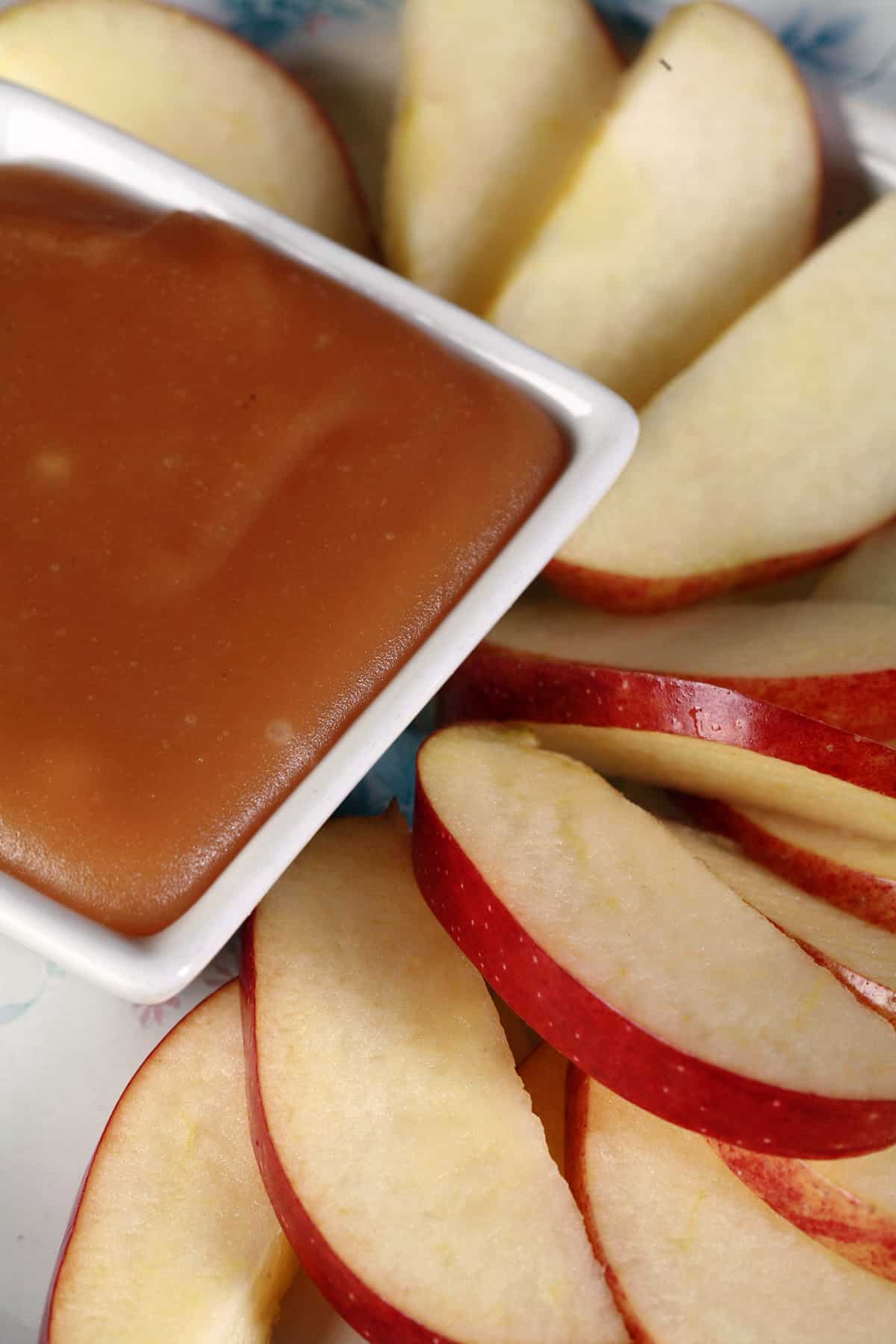 A plate of apple slices surrounding a bowl of maple syrup caramel.