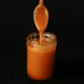 A spoon drizzlng maple caramel back into a jam jar.
