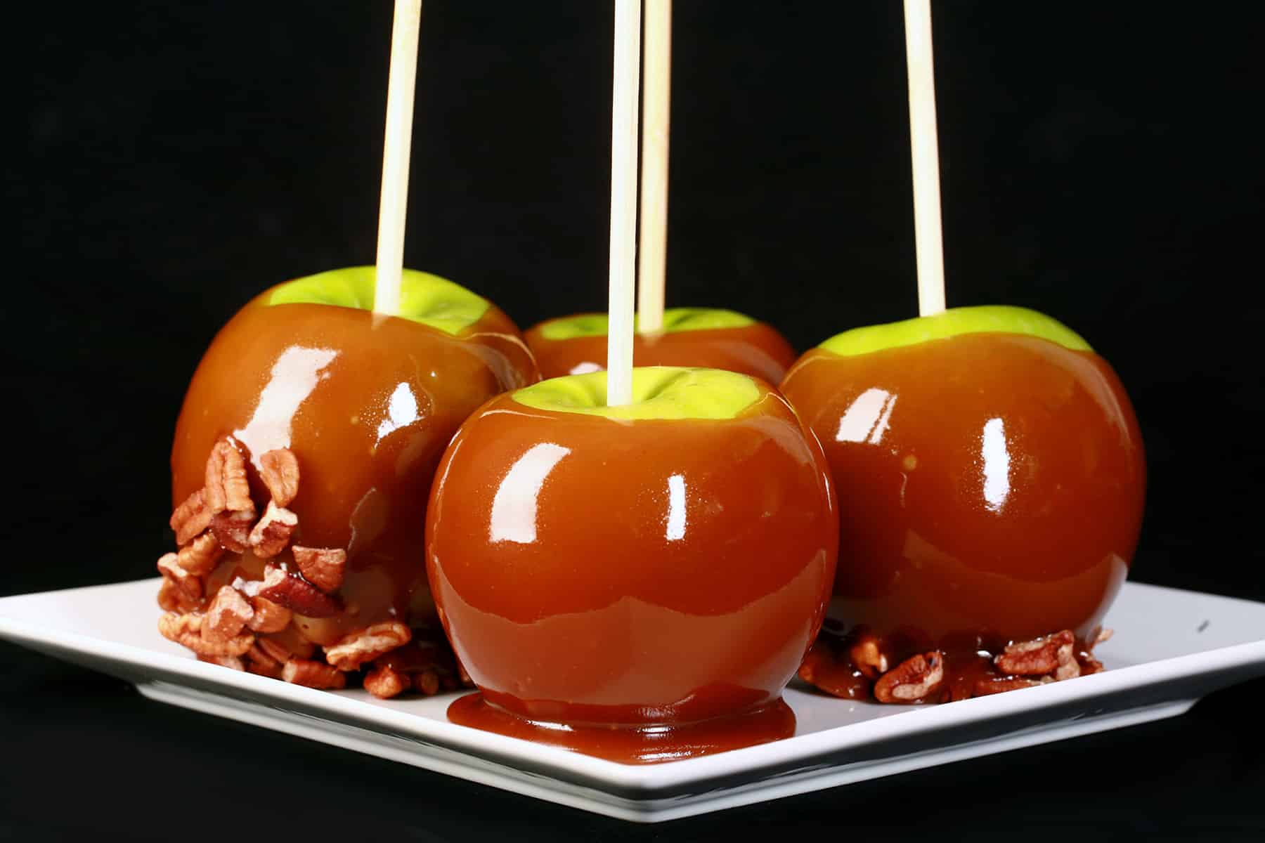 A plate of 4 maple caramel apples, 2 of which are dipped in chopped pecans.