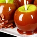 A plate of 4 maple syrup caramel apples, 2 of which are dipped in chopped pecans.