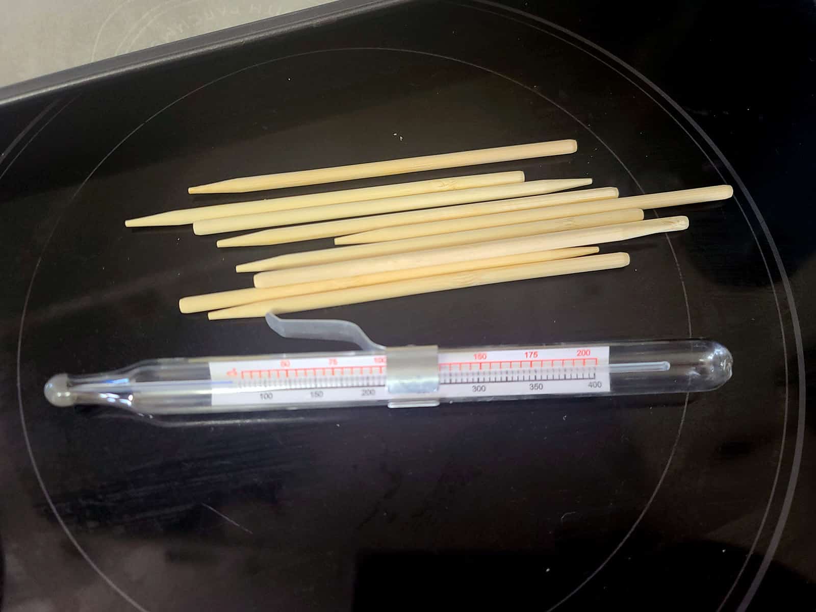 Wooden candy apple sticks and a candy thermometer on a stove top.