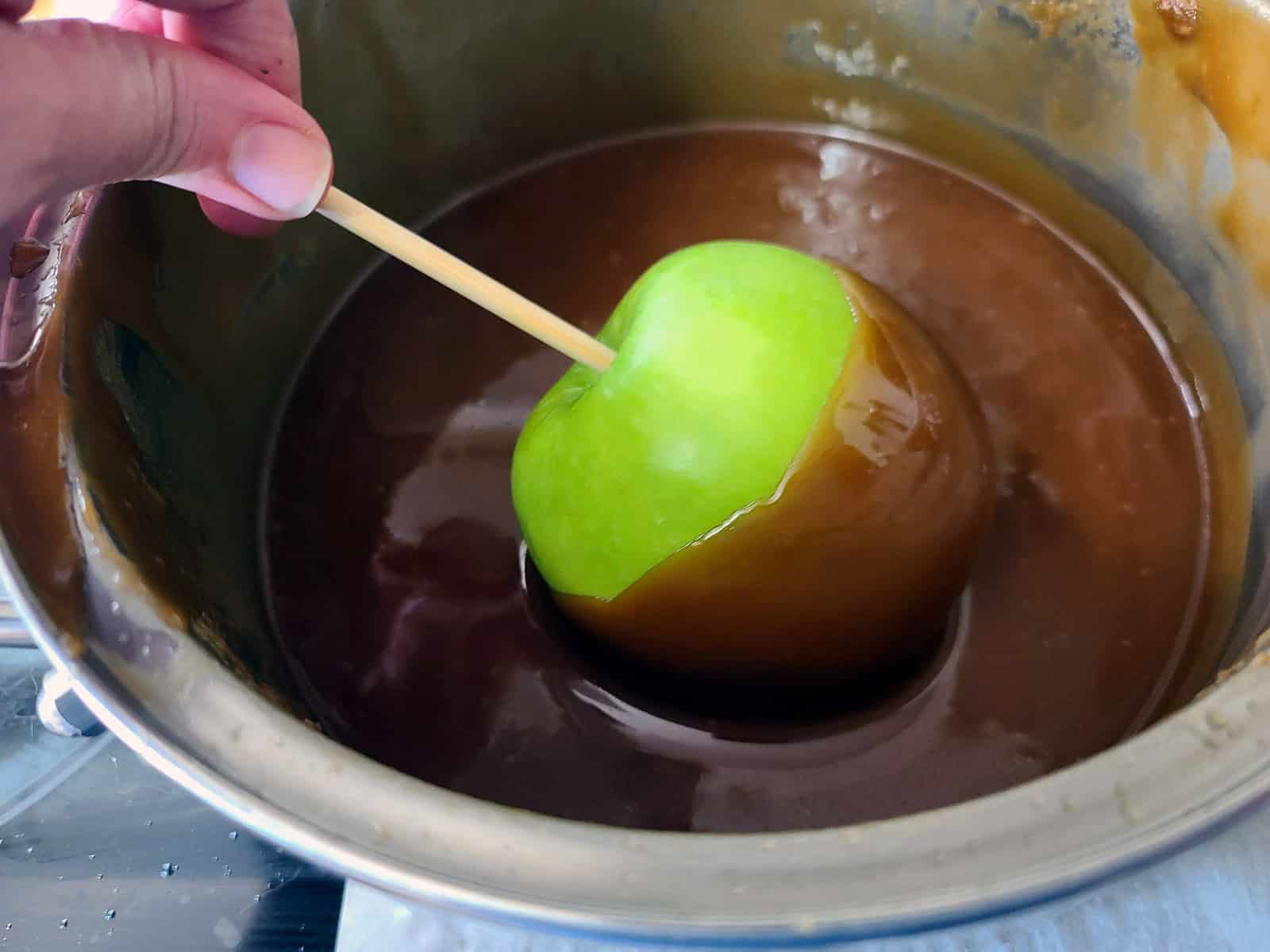 A green apple is being dipped in maple caramel.
