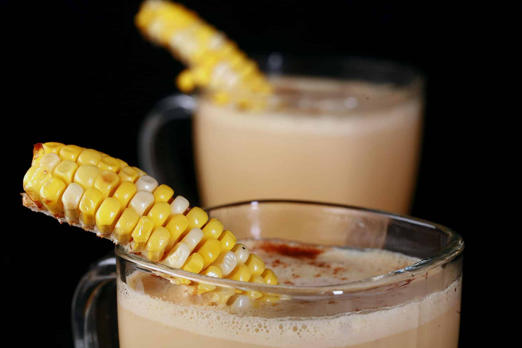 2 glass mugs of con cappuccino, garnished with narrow lengths of corn on the cob.