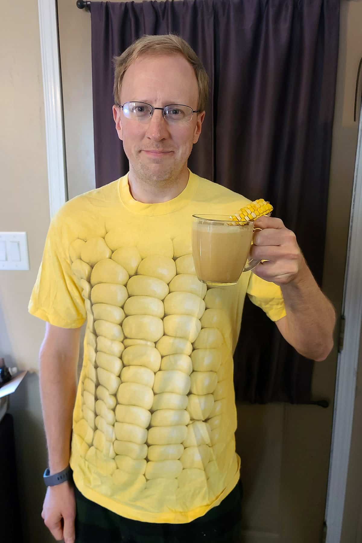 A middle aged white man in a corn shirt holding a mug of corn on the cobbuccino.