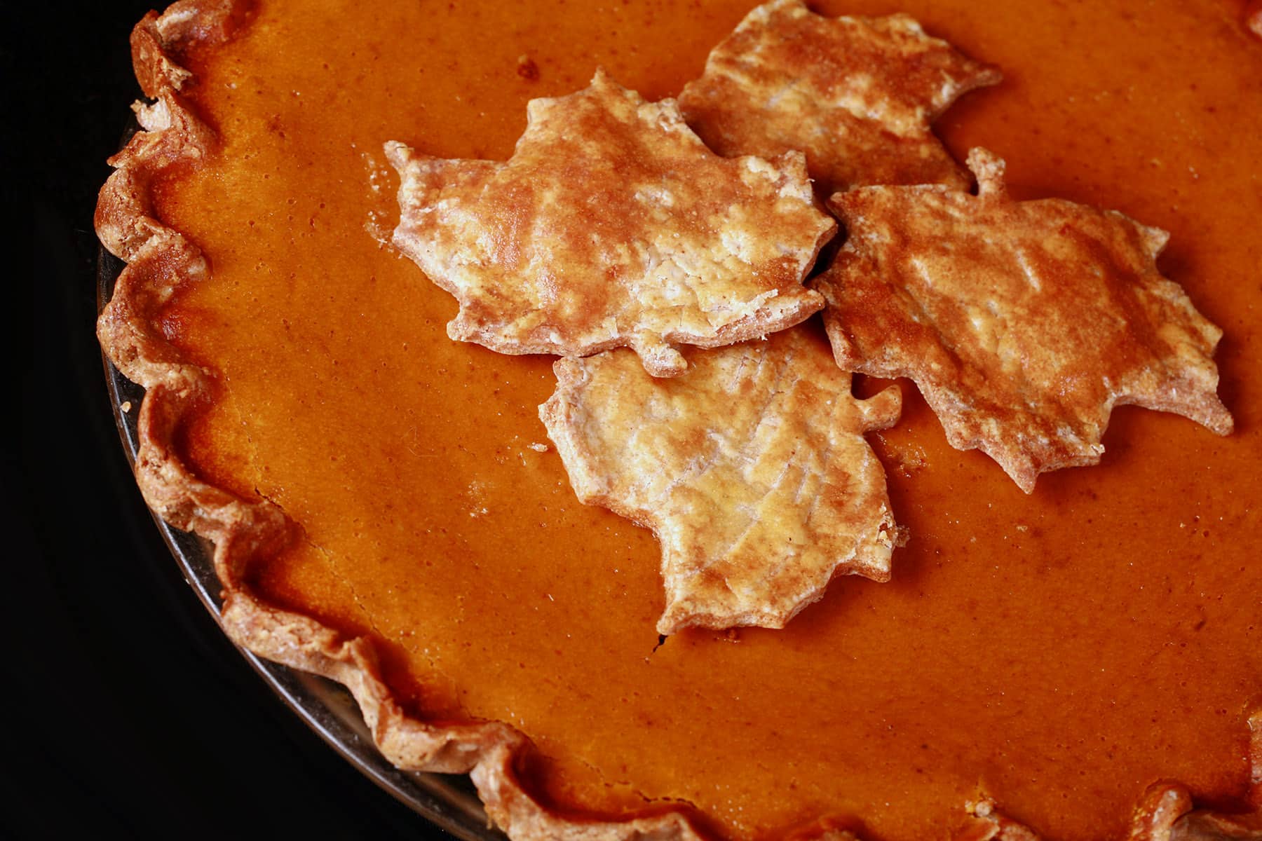 A close up view of the top of a gluten free pumpkin pie, topped with gluten-free pie crust maple leaves.