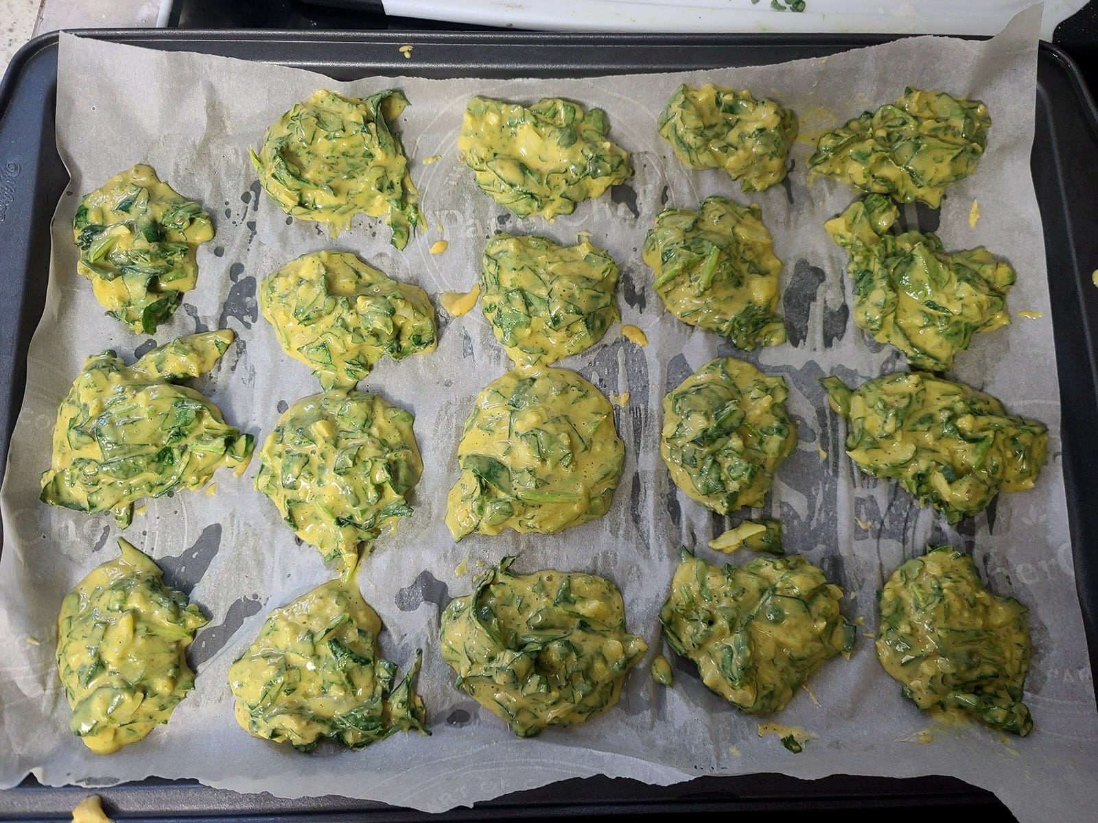 A parchment lined baking sheet with globs of palak pakoda batter spooned onto it.