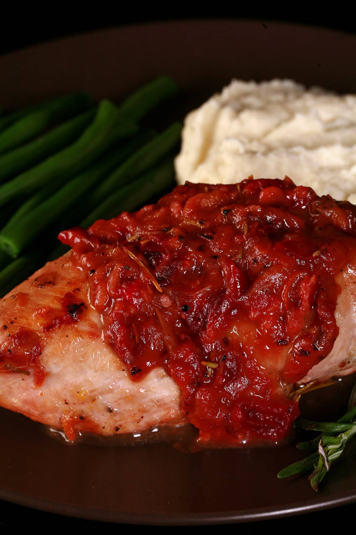 A serving of cranberry chicken on a plate with green beans and mashed cauliflower.